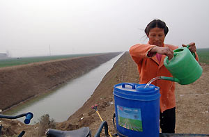 A Chinese woman pours water into her container near a newly dug aqueduct in Xiangfan, China's Hubei province March 6, 2006. Premier Wen Jiabao told parliament on Sunday that China would channel its surging economic growth to improve living conditions of rural people and narrow the widening gap between the country's rich cities and restive countryside.